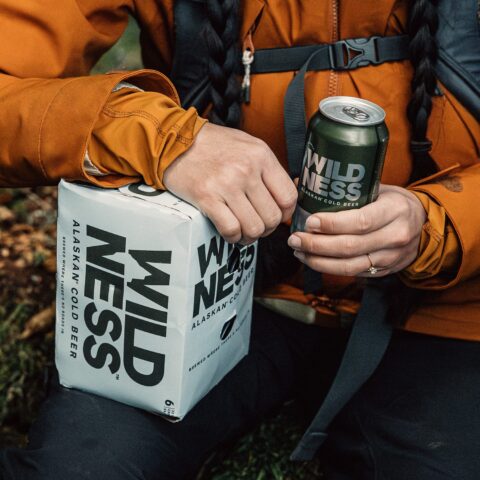 a woman's hands holding a box of WILDNESS beer and beer can